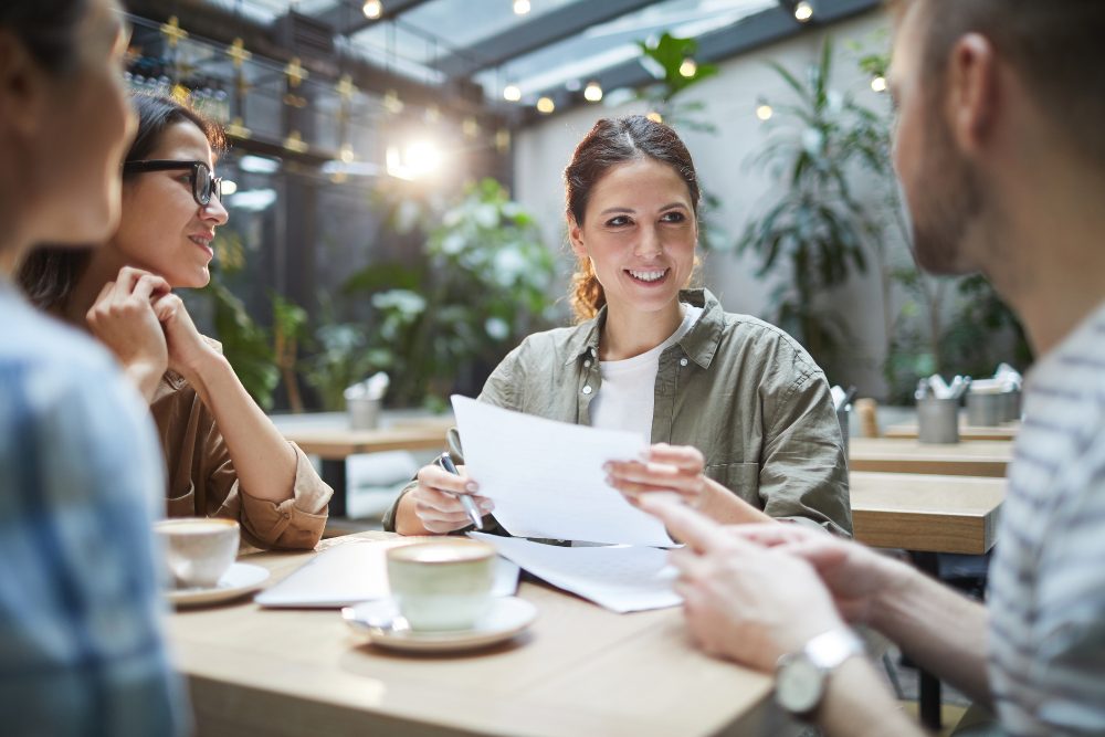 A business leader in conversation with her team over coffee and printed notes